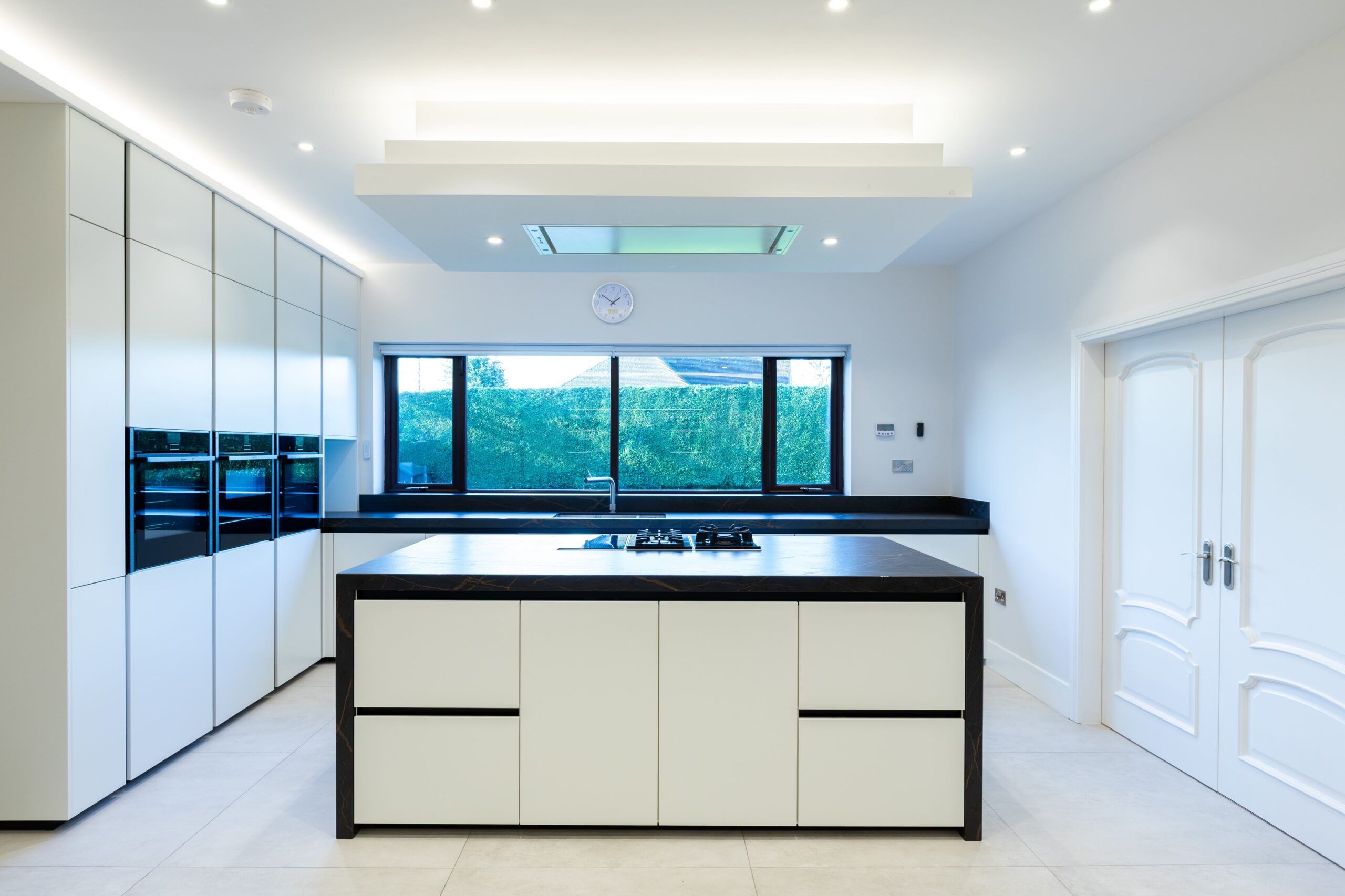 Modern white handleless German kitchen with island, skylight and integrated appliances