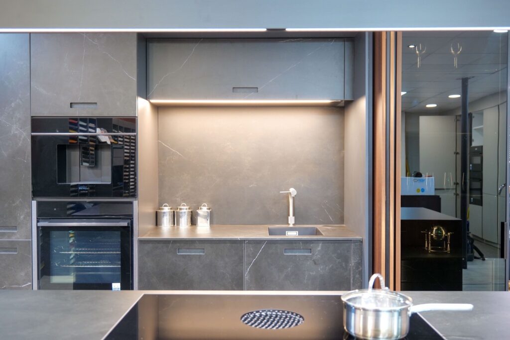 Dark grey stone-effect handleless kitchen with integrated coffee machine, wine cooler and recessed lighting — Suga Küchen showroom display