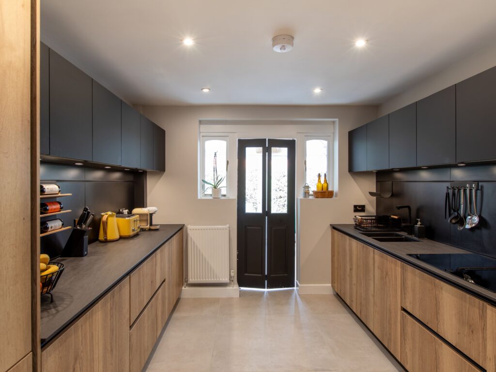 Galley style kitchen with matte black wall units, oak base cabinets and black worktops by Suga Kuchen