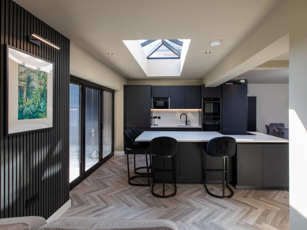 Dark navy handleless kitchen extension with skylight, marble island, bar stools and parquet flooring by Suga Kuchen