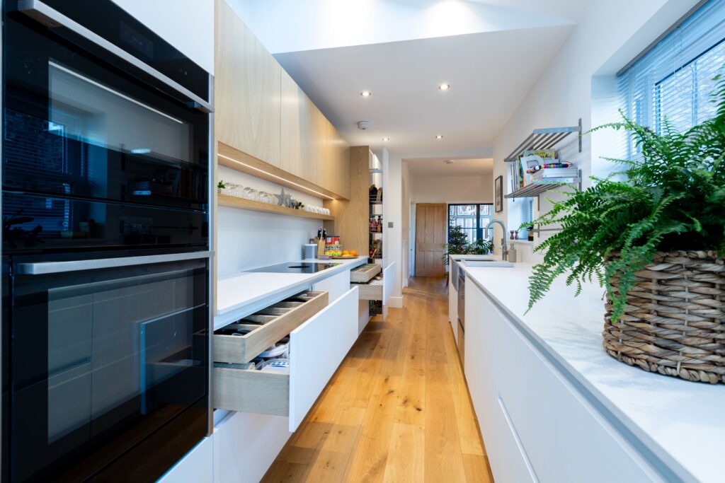 Modern handleless kitchen extension with white base units, wooden wall cabinets, open drawers and oak flooring by Suga Kuchen
