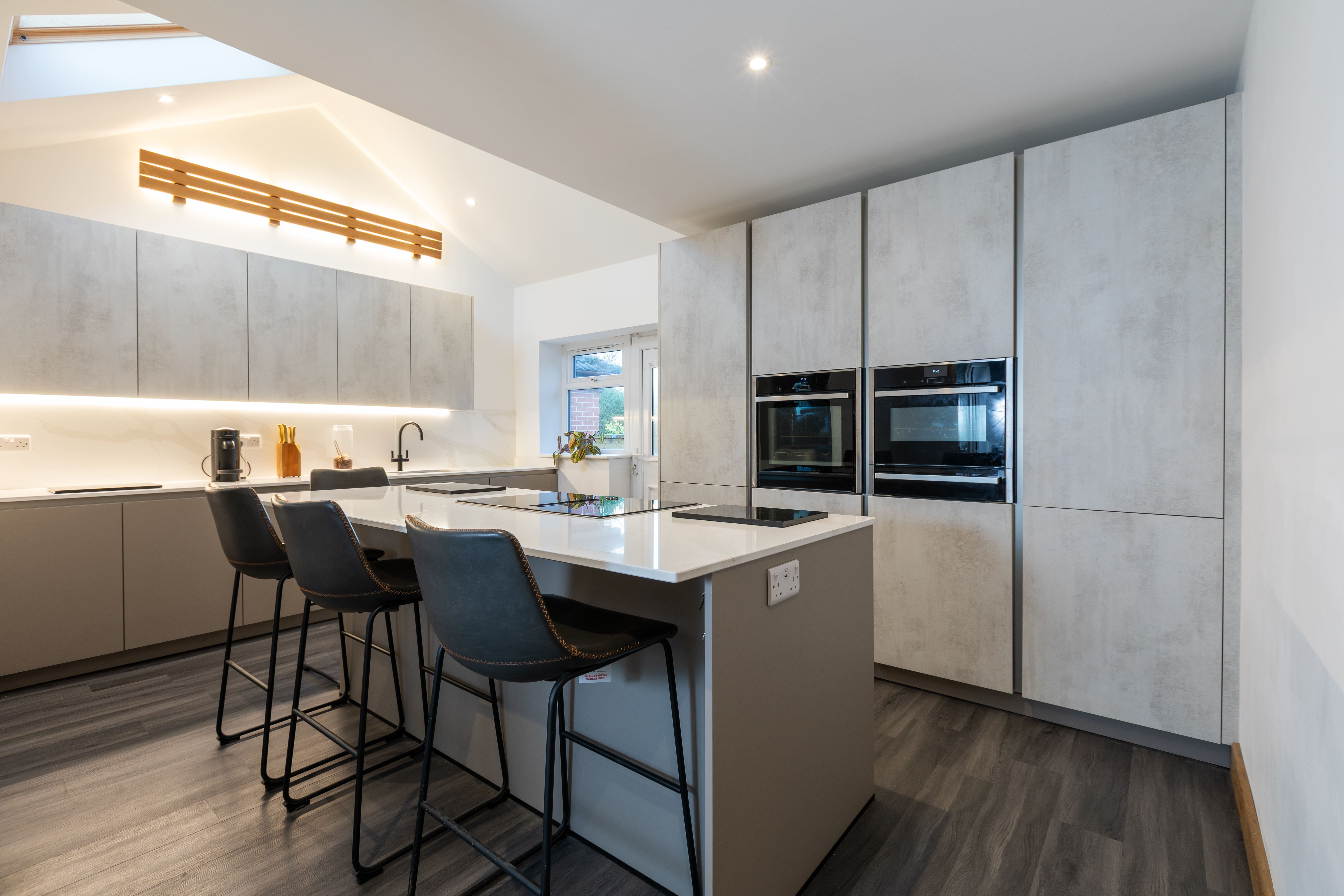 Contemporary grey handleless kitchen with breakfast bar, integrated ovens and LED lighting