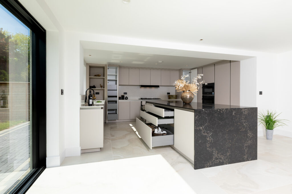 Open-plan modern kitchen with island drawers and dark stone worktop by Suga Küchen